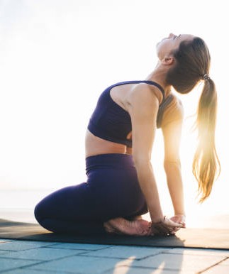 Side view of flexible barefoot lady performing Thunderbolt pose with hands together behind back and bending back during workout on beach